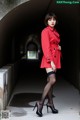 A woman in a red coat and black stockings posing for a picture.