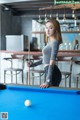 A woman standing next to a pool table holding a cue.