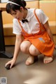 A woman in an orange apron crouching down on the floor.