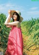 A woman in a pink dress and a straw hat standing in a field.