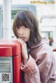 A young woman leaning against a red post box.